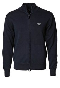 Navy blue knitted zip-up cardigan with ribbed cuffs and hem, standing collar, and small GANT logo on left chest.