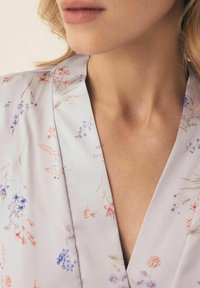 Sukienka w kwiatowy wzór w jasnoszarym materiale z dekoltem w kształcie litery V, z pastelowymi kwiatami i delikatnymi akcentami botanicznymi.