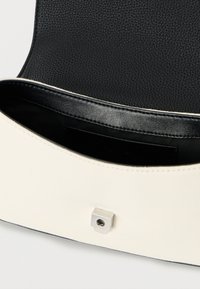 Μαύρο εσωτερικό από δερμάτινη υφή με εξωτερικό από κρεμ ύφασμα. Διαθέτει ασημί τετράγωνο κούμπωμα στην πρόσοψη. Απλός, σύγχρονος σχεδιασμός.