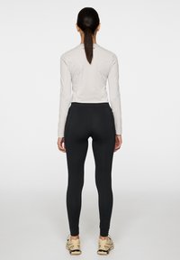Ljusgrå långärmad topp med texturerad design och svarta högmidjade leggings, tillsammans med beige sportskor, sedd bakifrån.