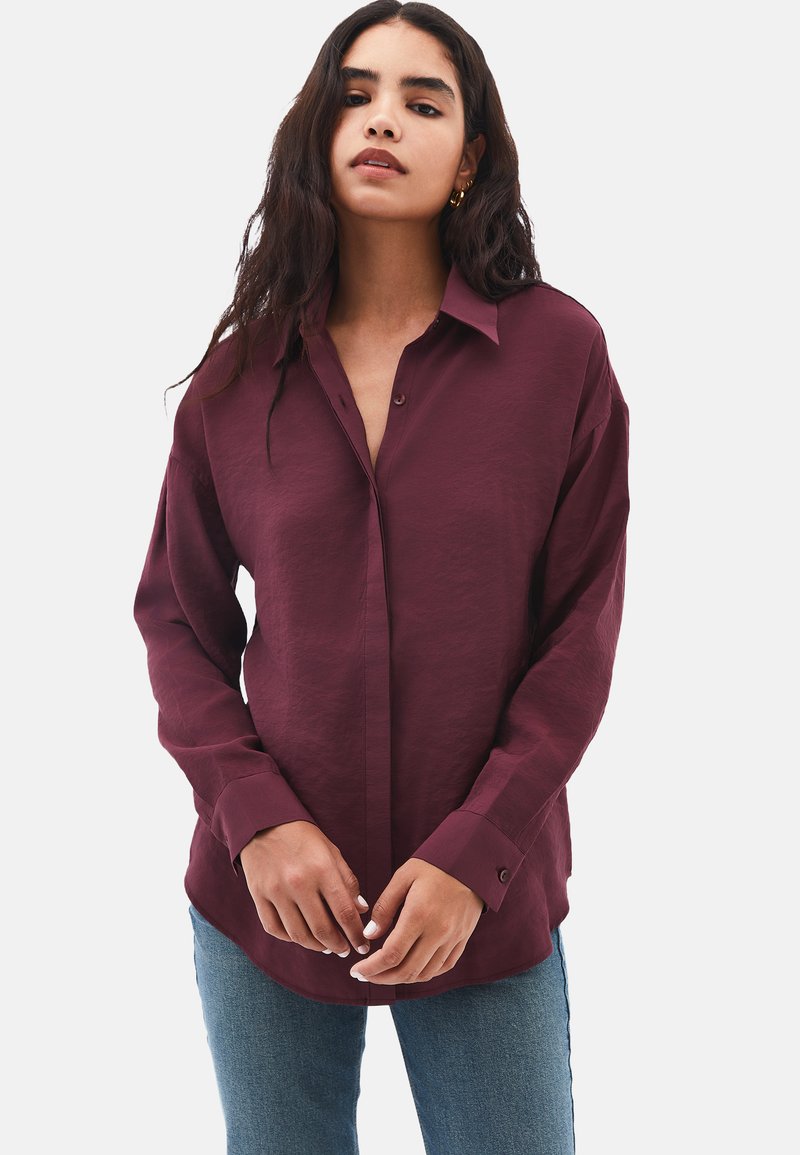 Camicia button-up bordeaux con vestibilità rilassata, maniche lunghe e colletto. Tessuto liscio, caratterizzato da un design classico e una lucentezza sottile.