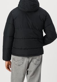 Black padded jacket with a hood, featuring horizontal stitching and a smooth texture. Paired with light gray denim pants.