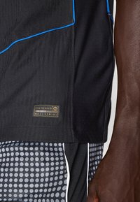 Maglietta atletica nera con texture a coste, cuciture di accento blu e un'etichetta con la scritta "ENGINEERED". Abbinata a pantaloni corti neri con motivo a pois.
