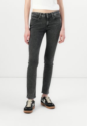 Jeans neri slim fit in denim strappato con cinque tasche e chiusura a bottone. Indossati con sneakers nere e bianche su uno sfondo neutro.