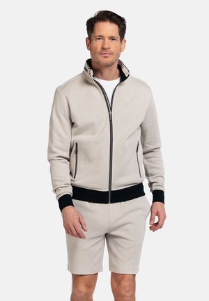 Lichtbeige zip-up sweatshirt met zwarte accenten en ritsen, voorzien van een hoge kraag en ribgebreide manchetten. Gecombineerd met bijpassende shorts.