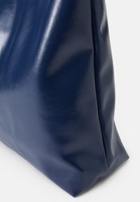 Granatowa torba z faux skórki o błyszczącej fakturze, kanciastym kształcie i złożonym designie. Charakteryzuje się minimalnymi detalami i gładką powierzchnią.