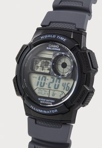 Montre numérique Casio avec boîtier en résine noire et bracelet en caoutchouc gris. Les caractéristiques incluent un écran LCD, plusieurs boutons et une résistance à l'eau jusqu'à 100 m.