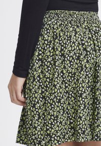Gonna nera con cintura elastica arricciata, decorata con un motivo floreale in verde e bianco. Tessuto liscio, lunghezza al ginocchio.