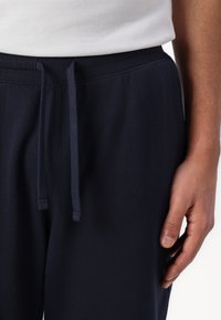 Pantalones de chándal de algodón en color navy con cintura elástica y cordón. Muestra una mano reposando sobre la tela, destacando su suave textura y ajuste entallado.