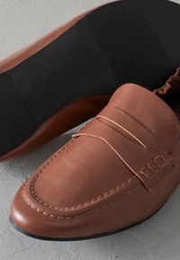 Mocassini in pelle marrone con una texture liscia, caratterizzati da una fascia decorativa cucita e una suola in gomma nera con un design rigato.
