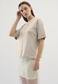 Beige színű pamut póló rövid ujjakkal és laza fazonnal, áttetsző, flitteres szoknyával párosítva, amely réteges textúrát mutat be.