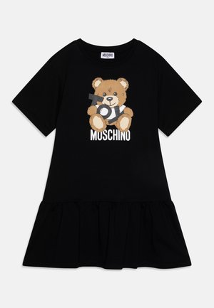 Czarna sukienka z krótkim rękawem i falbaną na dole, z motywem brązowego misia trzymającego listy oraz białym napisem „MOSCHINO” z przodu.