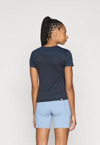 Marineblå trenings T-skjorte med korte ermer, med en glatt tekstur og et kontrasterende panel bak, satt sammen med lyseblå shorts.