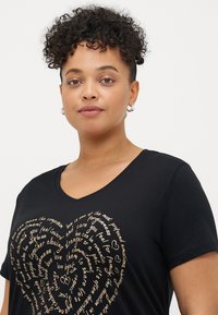 Μαύρο t-shirt με V λαιμόκοψη και χρυσό κείμενο σε σχήμα καρδιάς, με απαλό υλικό και κοντά μανίκια. Μινιμαλιστικός σχεδιασμός χωρίς επιπλέον γραφικά.