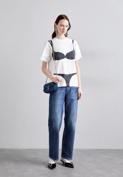White short-sleeve t-shirt with black printed bra and panty design, paired with blue straight-leg jeans and a small blue handbag. Black heels.