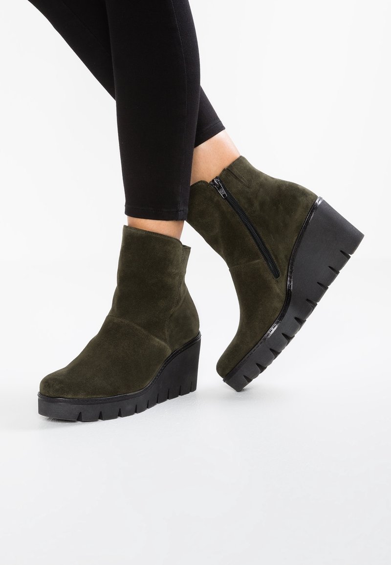 Bottines en daim vert à talon compensé avec une fermeture éclair visible, dotées d'une semelle noire texturée et d'un design épuré.