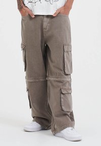 Kaki cargo-panten, met meerdere grote zakken, een relaxte pasvorm en een licht gestructureerde stof. Gecombineerd met witte sneakers.