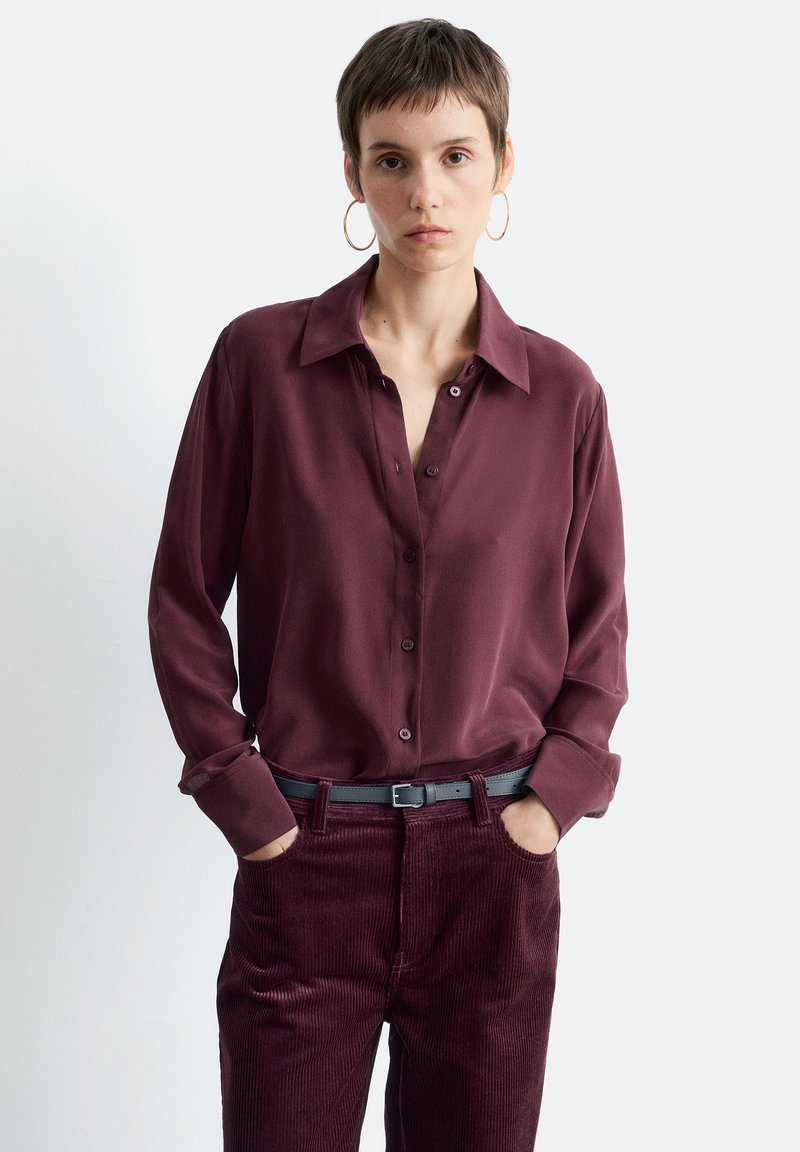 Burgundy silk blouse with a button-down front, pointed collar, and long sleeves, paired with matching corduroy pants and a black belt.