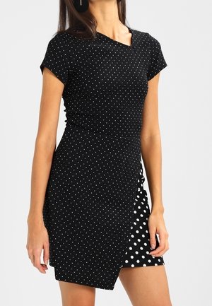 Czarna sukienka w grochy z krótkimi rękawami, z dopasowanym górnym partem i asymetryczną spódnicą z większymi białymi groszkami. Gładka faktura tkaniny.