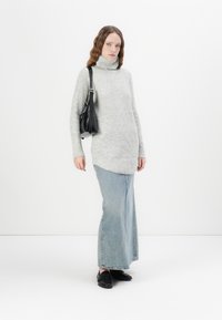 Grey knitted turtleneck sweater, long fit, paired with a light blue denim maxi skirt. Model carries a small black handbag and wears black shoes.