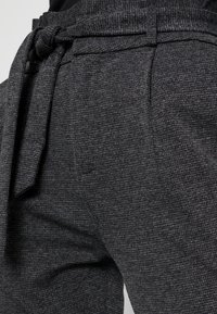 Pantalons texturés gris avec un détail de taille nouée, coupe droite et motif subtil, adaptés à la fois pour un look décontracté et formel.