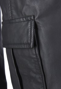 Close-up van zwarte leren broek met een zijzak met gestikte randen, een gladde textuur en een subtiele glans. Gedetailleerde stiksels zichtbaar.