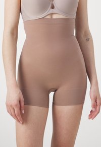 High-waisted shaping shorts made from stretchy tan fabric, designed for smooth contouring; features a seamless leg and a mid-thigh cut.