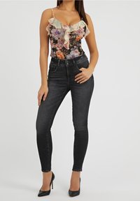 Bodysuit floral con escote con volantes en negro, combinado con jeans oscuros de tiro alto. La modelo lleva tacones de aguja negros.