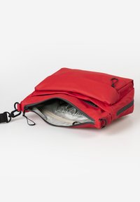 Rote Stofftasche mit einem offenen Reißverschluss, der ein graues Innenfutter und elastische Aufbewahrung offenbart. Verfügt über einen verstellbaren Trageriemen und schwarze Hardware-Akzente.