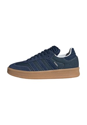 Navy blauwe Adidas Samba sneaker met rubberen zool, drie strepen, gestructureerd bovenwerk en de tekst "SAMBA" aan de zijkant.