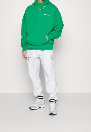 Groene hoodie, grijze joggingbroek met logo en grijze sneakers met zwarte en mintaccenten. Hoodie heeft een voorzak; losse pasvorm.