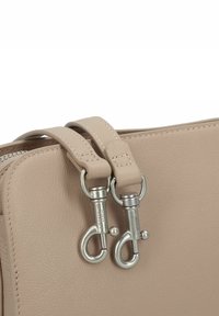Beige Lederhandtasche mit zwei Reißverschlussanhängern, metallischen Akzenten und strukturiertem Oberflächenmaterial. Besondere Merkmale sind die Steppnähte an den Griffen.