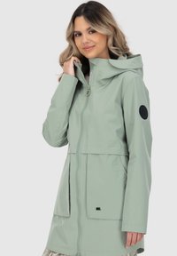 Helle grüne, kapuzenbehangene Regenjacke aus glattem, wasserdichtem Material, mit einem Frontreißverschluss, Seitentaschen und einem schwarzen, runden Logopatch.