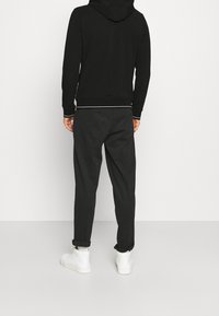 Felpa nera con tasca a marsupio frontale, cordoncino bianco e polsini a contrasto. Indossata con pantaloni scuri leggermente affusolati e sneaker bianche.