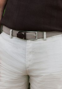 Woven light brown belt with dark brown leather accents, paired with light beige linen pants featuring a textured finish.