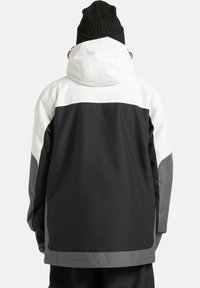 Giacca impermeabile nera, bianca e grigia con cappuccio; presenta un design a blocchi di colore, una vestibilità comoda e tessuti testurizzati sulle maniche.