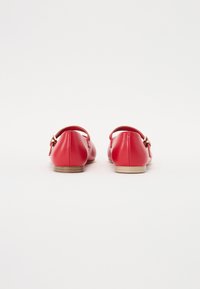 Bailarinas de cuero rojo con punta redonda, que presentan una pequeña correa y un detalle de hebilla dorada. La suela es beige, complementando el diseño en general.