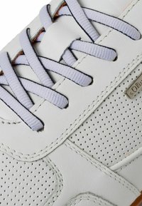 Weiße Sneaker mit perforierter Oberfläche, helllila Schnürsenkeln und schwarzen Stickdetails. Verfügt über ein markiertes Metalletikett an der Seite.