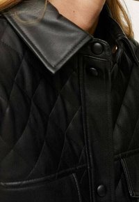 Czarna pikowana kurtka z skórzanym kołnierzem, z zatrzaskami i teksturowanym wzorem materiału, który dodaje wizualnego zainteresowania i trwałości.