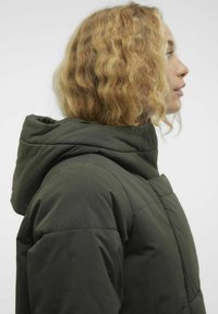 Chaqueta acolchada de color verde oscuro con un alto cuello y capucha adjunta, con un diseño acolchado que proporciona aislamiento. Textura suave y mate.