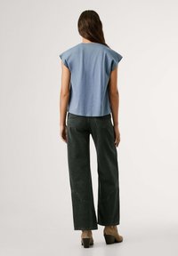 Gaiši zils kokvilnas tops ar kapu piedurknēm, savienots ar augstās jostas vietas tumšajiem džinsiem ar izliektiem diega elementiem un masīmiem brūniem papēžiem.