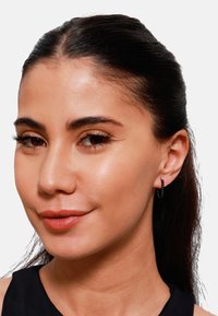 Sorte hoops-ører ring med små sfæriske detaljer, laget av polert metall, vist på en modell med mørkt hår og glatt hud.