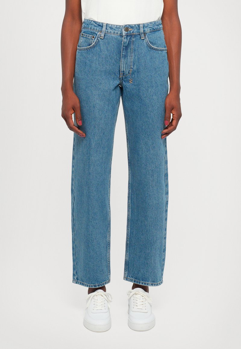 Light blue, high-waisted denim jeans with a straight leg and cropped hem. Features front pockets and a faded texture. Paired with white sneakers.