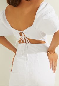 Abito bianco con tessuto testurizzato, maniche a sbuffo, schiena scoperta con dettagli in pizzo, e silhouette aderente. Linee pulite con accenti minimi.
