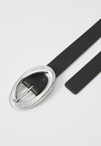 Black leather belt with a large silver oval buckle and a single prong. The strap is smooth, and the buckle features engraved branding.
