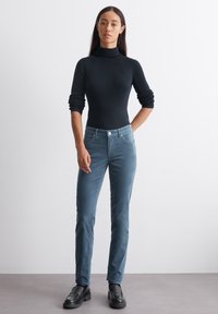 Čierny dlhý rukáv turtleneck sveter skombinovaný s svetlomodrými priliehavými kordovým nohavicami a čiernymi mohutnými loafers. Hladká textúra, minimálne detaily.