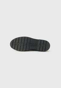 Black rubber shoe sole with a textured grip, featuring horizontal grooves and embossed brand name "CALVIN KLEIN" across the bottom.