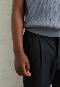 Hallgrey kaetud sviiter, millel on kudumismuster ja ribidega ääred, koos mustade täpselt lõigatud pükstega, millel on küljetaskud ja sile viimistlus.