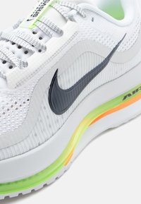 Ναϊκ sneakers με άσπρο δικτυωτό πάνω μέρος και γκρι λεπτομέρειες, χαρακτηριστικό σήμα Nike και πολύχρωμο πάτο με αερο cushioning.