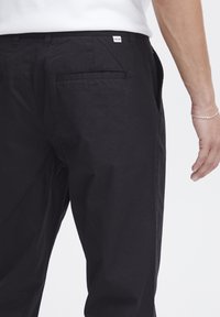 Pantaloni negri din bumbac cu un design drept, care includ buzunare laterale și buzunare pe spate, o textură subtilă și un eticheta mică cu logo pe talie.